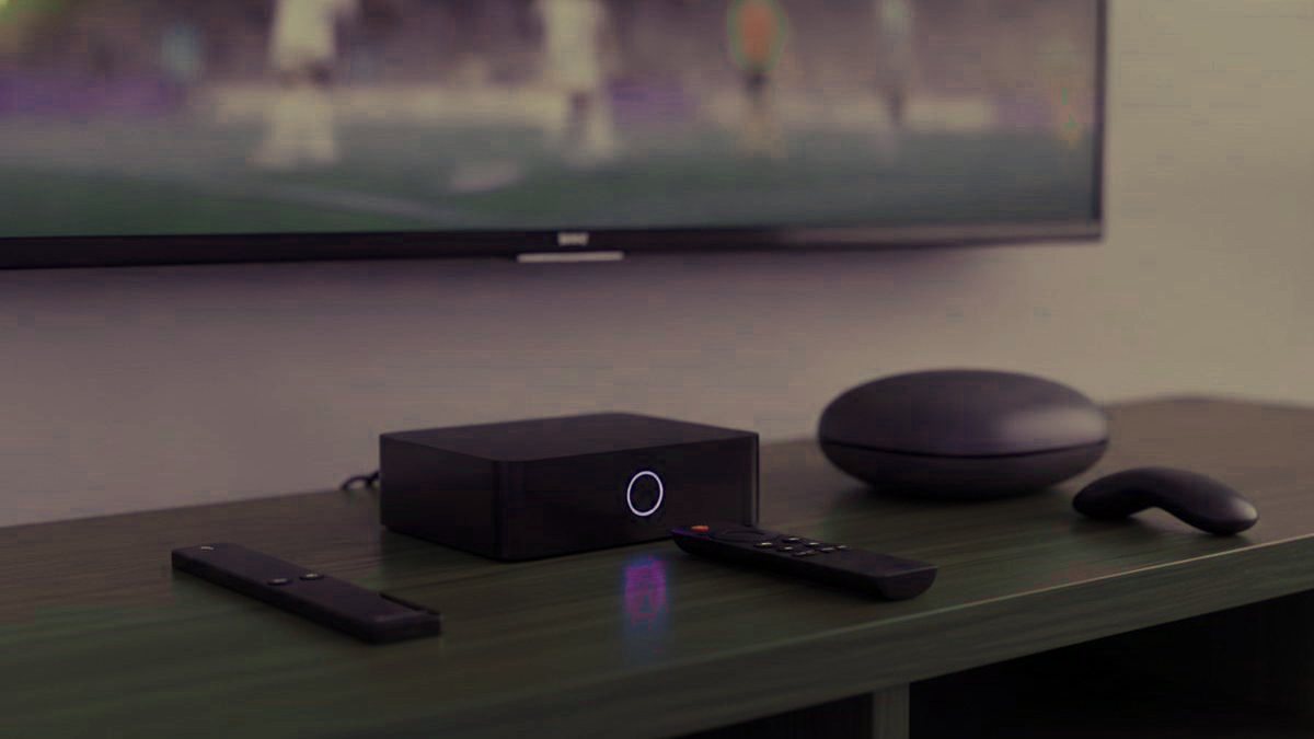 A streaming stick, a set-top box and a round streaming box with their remotes on a TV console